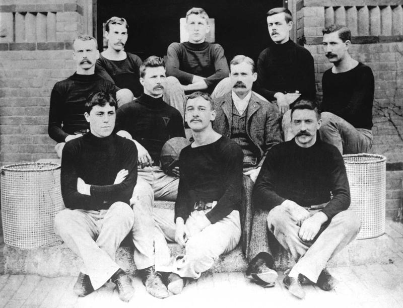 Džeimss Neismits (James Naismith, otrajā rindā pirmais no labās) ar pirmo basketbola komandu. Springfīlda (Masačūsetsas pavalsts), 1891. gads.