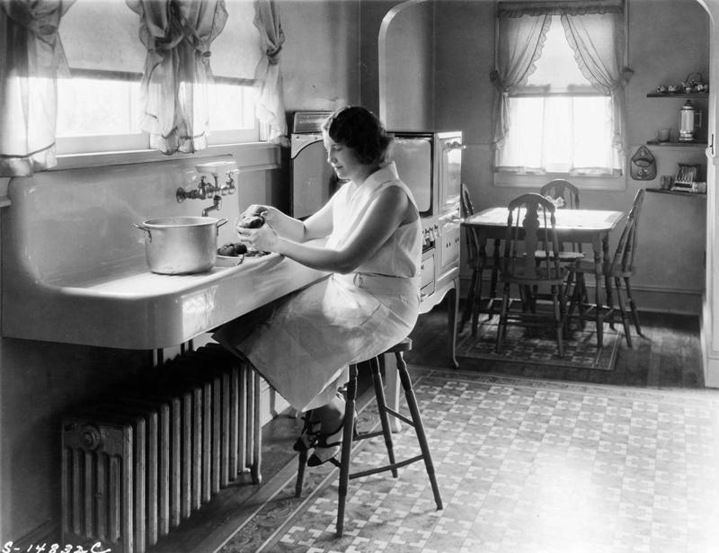 Sieviete mizo kartupeļus virtuvē pie izlietnes. ASV, 1925. gads.