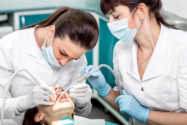 Zobārste un medmāsa pacientei veic zobu tīrīšanu zobārstniecības kabinetā. 2014. gads.