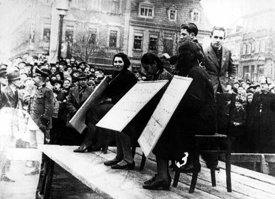 Ebreju sievietes tiek publiski izstādītas ar kartona izkārtni kaklā, kurā teikts: “Es esmu izslēgta no nacionālās kopienas (Volksgemeinschaft)” pret ebrejiem vērstā pogroma laikā, kas pazīstams kā “Kristāla nakts” (Kristallnacht). Linca, Austrija, 11.1938.