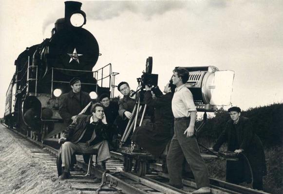 Kreisajā pusē sēž režisors Leonīds Leimanis, aiz viņa stāv Rolands Kalniņš, pie kameras Vadims Mass, priekšplānā Haralds Ritenbergs (Nauris) filmas "Nauris" uzņemšanas laikā. 1957. gads.