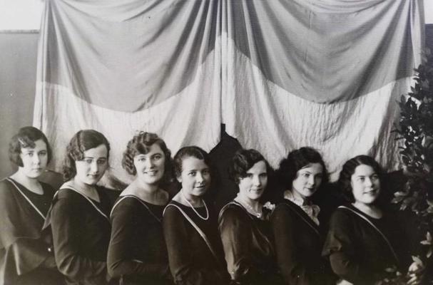 Daļa no korporācijas "Selga" dibinātājām pie iesvētītā karoga, 02.1927. No kreisās: Flora Zariņa-Austruma, Alma Ventere-Millere, Emma Damberga, Marta Rullīte, Alīda Graudule, Erna Priede-Jansone un Austra Jurkovska-Cīce.