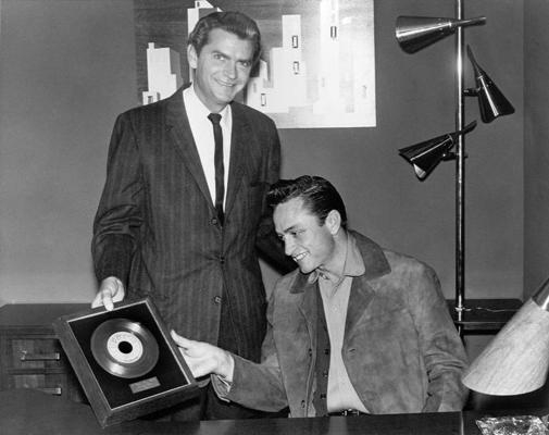 Atzīmējot pārdošanas panākumus, Sun Records dibinātājs Sems Filipss mūziķim Džonijam Kešam sniedz ierāmētu singlu “I Walk the Line”, 1956. gads, Memfisa, ASV.