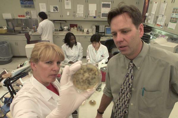 Medicīnas epidemiologs Daglass Frajs (Douglas M. Frye) un mikrobioloģe Džoana Stērdžena (Joan Sturgeon) aplūko pārtikas paraugus ar listērijām no tītara un siera sviestmaizēm. ASV, 2001. gads.