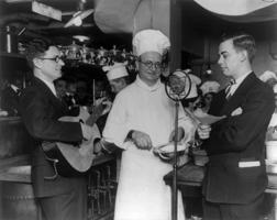 Čikāgas radio stacija WLS raida no viesnīcas virtuves. Pie mikrofona (no kreisās) dziedātājs Bredlijs Kinkeids (Bradley Kincaid), pavārs Toms Maligeino (Tom Magliano) un diktors Bobs Boltons (Bob Boulton). Čikāga, ASV, 1929. gads.