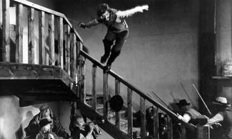 No kāpnēm ar zobenu rokās lec Pēteris (Artūrs Ēķis) filmā "Vella kalpi", 1970. gads.
