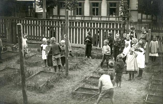 Augusta Dombrovska organizētā bērnudārza Vecmīlgrāvī audzēkņi un audzinātājas dārza darbos. 20. gs. 20. gadi.