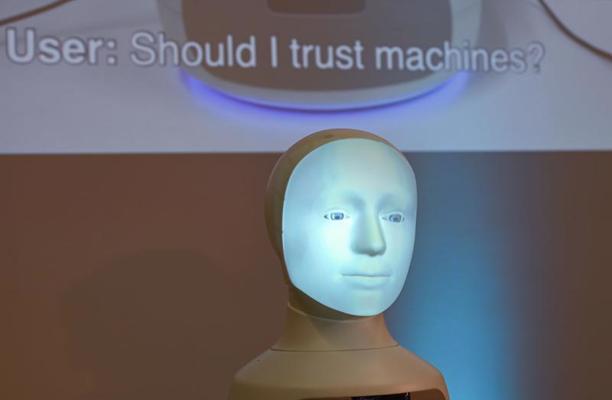 Mākslīgā intelekta tehnoloģiju radīts robots un morāles izvēles mašīna "Alfie", aiz tā uz sienas tiek projicēts jautājums "Lietotājs: vai man jāuzticas mašīnām?". Darmštate, Vācija, 31.08.2020.