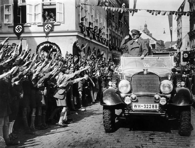 Ādolfa Hitlera sagaidīšana Vācijas karogiem izrotātā ielā Sudetijā, Vācijas okupētajā Čehoslovākijas teritorijā. 1938. gads.