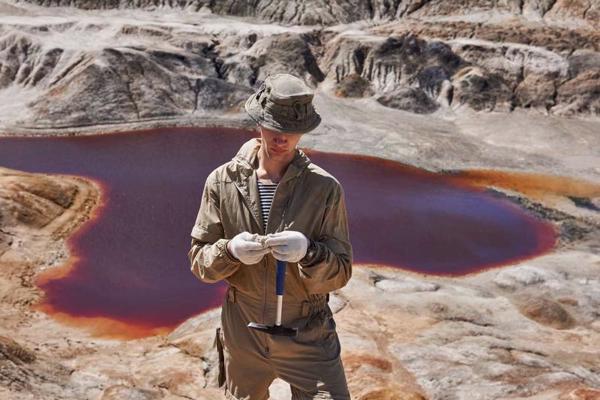 Ģeologs pēta minerāla paraugu pie kanjona ar sālsezeru. 2020. gads.