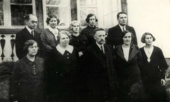 Otrajā rindā pirmais no kreisās: mācītājs un ticības mācības skolotājs Oskars Sakārnis Aizputes vidusskolas skolotāju vidū. 03.12.1935.