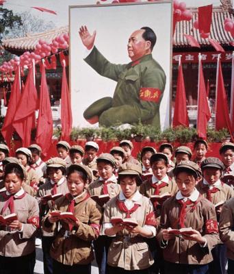 Bērni formās lasa Mao Dzeduna Mazo sarkano grāmatu, aiz viņiem Mao Dzeduna attēls. Ķīna, ap 1968. gadu.