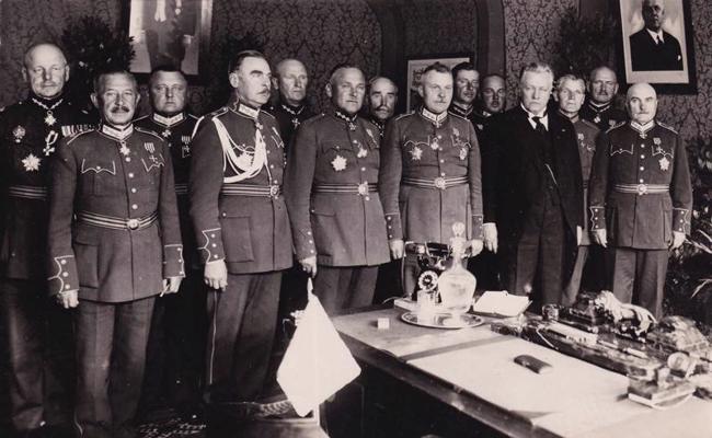 Latvijas armijas štāba priekšnieks ģenerālis Mārtiņš Hartmanis (priekšējā rindā otrais no kreisās) kopā ar armijas komandieri ģenerāli Krišjāni Berķi (priekšējā rindā ceturtais no kreisās), kara ministru ģenerāli Jāni Balodi (priekšējā rindā piektais no kreisās) un citiem armijas augstākajiem virsniekiem darba kabinetā J. Baloža dzimšanas dienā. 1936. gads.
