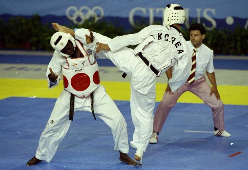 1988. gada olimpisko spēļu taekvondo demonstrācijā korejietis Kims Džongsoks (김종석) uzbrūk Emanuelam Ogenedžobo (Emmanuel Oghenejobo) no Nigērijas. 1988. gada olimpiskās spēlēs Seulā, Dienvidkorejā.