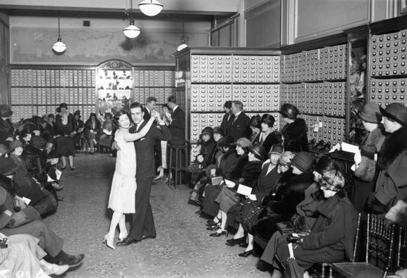 Klienti vēro pāri, kas dejo fokstrotu apavu veikalā. 1925. gads.